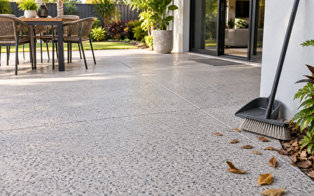 A broom and dustpan beside a clean textured concrete patio illustrate gentle routine care of a resurfaced area